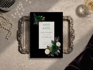 Emerald green floral save the date template shown on a grey surface with editorial flower artwork, pearl necklace and silver tray. Flowers include Emerald green roses, ivory roses, blue thistle, craspedia (billy buttons), pampas plumes and eucalyptus.