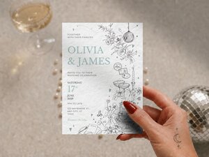 A hand holds a wedding invitation with travel-themed line art, featuring text for "Olivia & James" and event details.