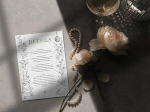 A details card with black text and line art illustrations of flowers and wedding items, next to a champagne glass, a pearl necklace, and a white rose.
