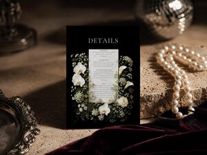 A details card with white floral graphics and text sits on a stone block near pearls and a silver tray.
