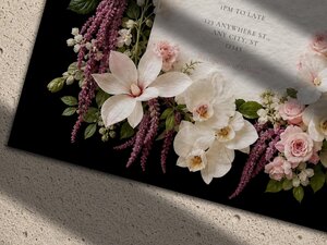 A close-up view of the corner of the wedding invitation featuring detailed pink roses, white orchids, and purple amaranthus flowers against a black background.