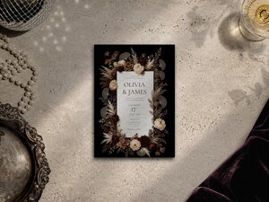 A flat lay shot of the wedding invitation centered on a light stone surface alongside a strand of pearls, a glass of champagne, and an ornate tray.