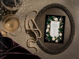 An overhead shot shows the wedding invitation inside an ornate vintage tray next to a string of pearls and a glass of champagne.