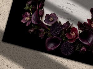 Close-up detail of a wedding invitation featuring dark plum and burgundy floral arrangements against a black background.