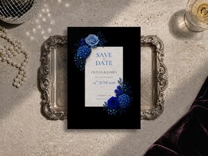 A Save the Date card featuring blue roses and berries sits centered on a decorative silver tray.