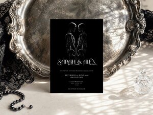 Gothic wedding invitation featuring romantic skeleton artwork, symbolic hand gestures and elegant dark romance styling on a black background.