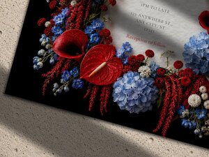 Close-up detail of a dark wedding invitation featuring a dense floral arrangement of red anthuriums, blue hydrangeas, and tiny white flowers.