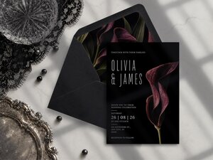 A black wedding invitation rests next to a matching dark envelope, styled on a surface with black lace and a silver tray.