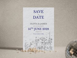 A Save the Date wedding card with blue text reading 14th June 2028, displayed with pearls and a disco ball.
