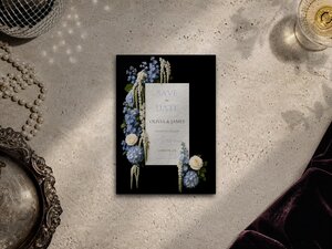 A wedding save the date card on a textured surface featuring blue and white flowers against a black background.