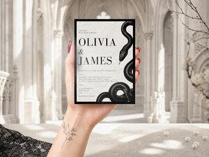 A hand holds up the black and white snake wedding invitation against a blurred architectural background.