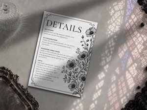 A wedding details card featuring botanical floral vines along the right border, placed beside an ornate tray and lace.