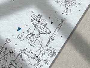 A close up macro shot of the wedding invitation line drawings shows a small figure swimming in a cocktail glass next to a tiered cake.