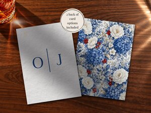 Two wedding cards showing a monogram on the front and a blue floral pattern on the back displayed on wood.