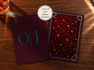 Two stationery cards with claret backgrounds and blue text sit on a wooden table near a glass of whiskey.