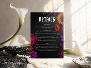 A black details card with colorful gothic floral corners, displayed vertically next to white calla lilies and a string of pearls.