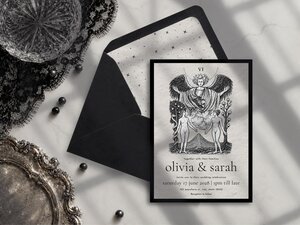 A tarot-style wedding invitation and its matching black envelope featuring a star-patterned liner, surrounded by gothic props on a white table.