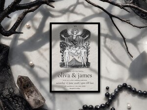 A tarot-themed wedding invitation card styled with a black border sits on a marble surface surrounded by dark branches, pearls, and a crystal.