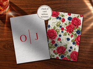 Two wedding stationery card options lie on a wooden surface, one showing red monogram initials and the other covered in a dense pattern of red and blue roses.