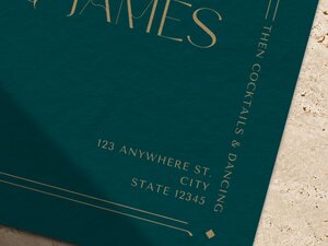 Close-up of the bottom corner of a dark teal wedding invitation showing gold serif text and thin line details.