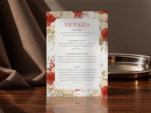 Wedding details insert card with floral corners, displayed vertically on a wooden table next to a silver tray.
