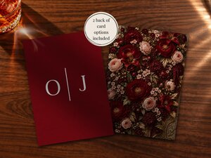 Two wedding card options displayed on a wooden table, one showing a dark red back design with initials and the other a floral front.