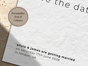 Close up of a save the date card on textured paper with minimal black text on a stone surface.