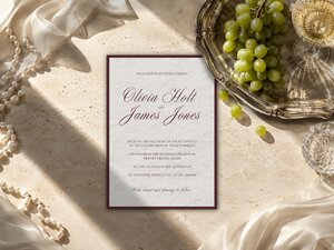 An overhead view of a wedding invitation template on a textured surface with draped fabric, grapes, and pearls.