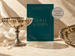 Dark teal wedding invitation card next to a silver pedestal bowl and tray on stone, decorated with loose pearls and grapes.