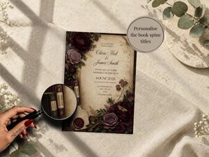 A magnifying glass hovers over miniature book spines on a wedding invitation featuring dark floral arrangements and vintage parchment paper.