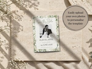 A save the date card rests on a stone surface, featuring a black and white photo of a couple surrounded by white flowers and a round text overlay on the right.