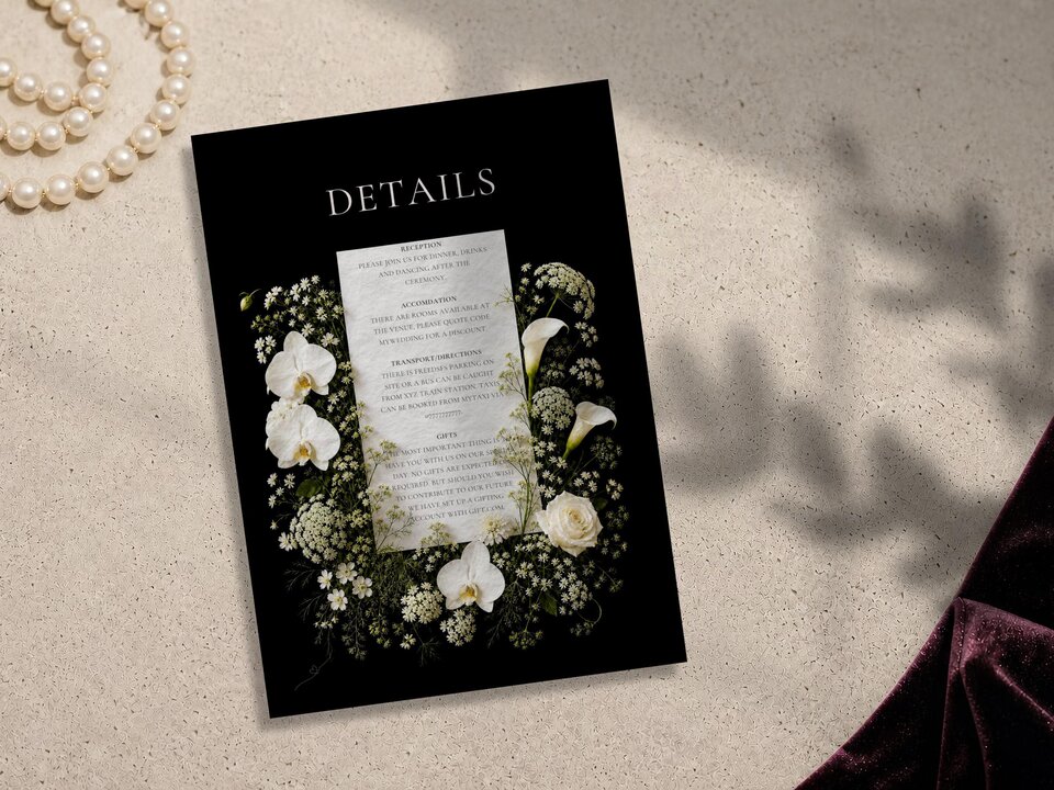 A black details card adorned with white orchids and floral elements sits flat on a textured surface.