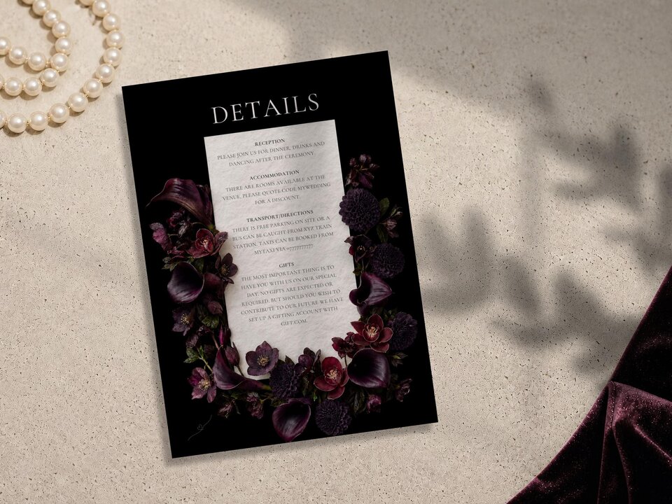 A wedding details card decorated with moody plum calla lilies and dahlias, resting on a stone background.