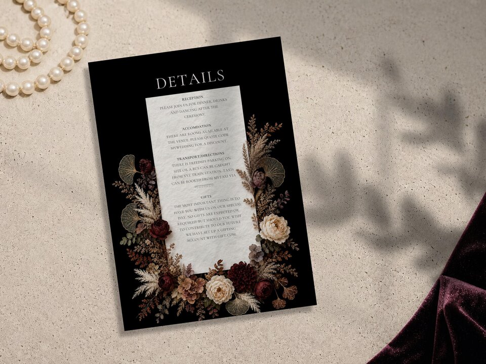 A wedding details card with a black background and a white text panel is placed flat on a neutral stone surface next to purple velvet fabric.