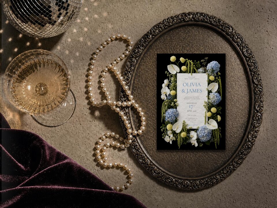 Blue and yellow floral wedding invitation featuring blue hydrangeas, white phalaenopsis orchids, white anthuriums, yellow pompon chrysanthemums and cascading green amaranthus on a dramatic black background.