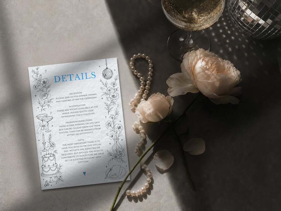 A wedding details card displayed on a stone surface with a strand of pearls, light pink roses, a champagne glass, and a disco ball.
