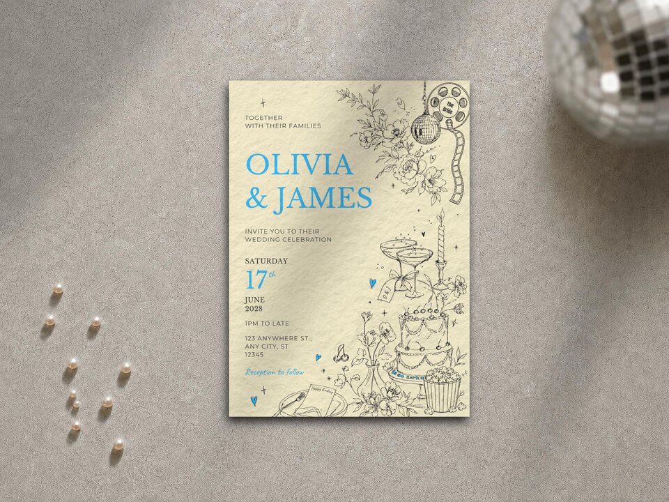 A single wedding invitation card centered on a neutral textured surface next to scattered pearls and a disco ball.