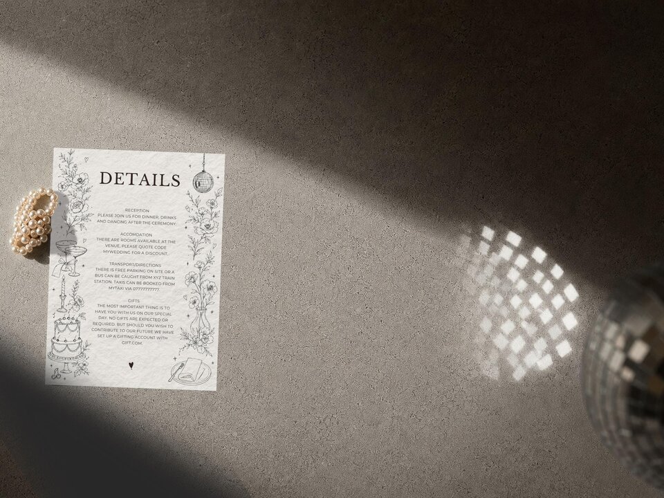 A wedding details card with black text and line art, placed on a concrete surface next to a pearl bracelet and a disco ball casting light patterns.