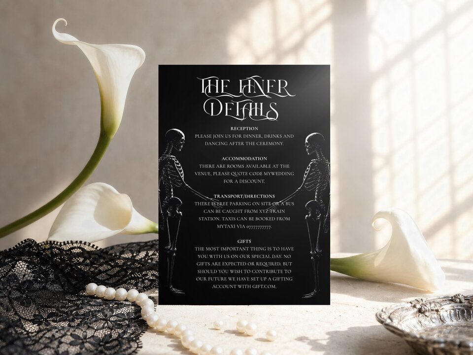 A black details card featuring gothic white text and skeleton figures on a white surface with white calla lilies and pearls.
