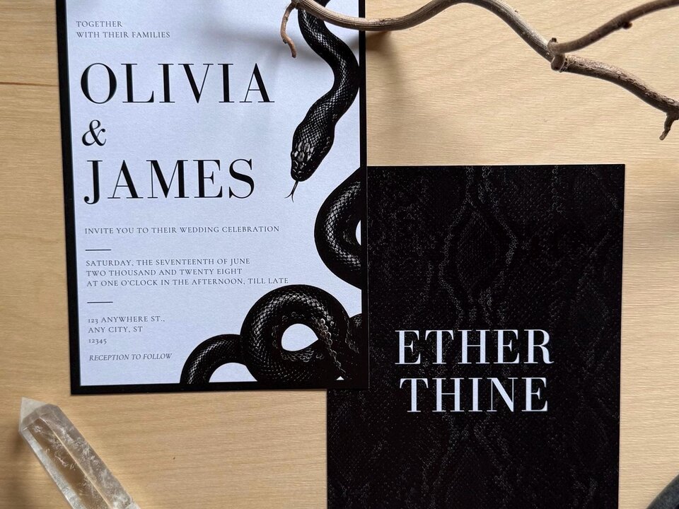 Two stationery cards displaying a snake design and a dark snakeskin pattern placed on a wooden tabletop with a crystal.