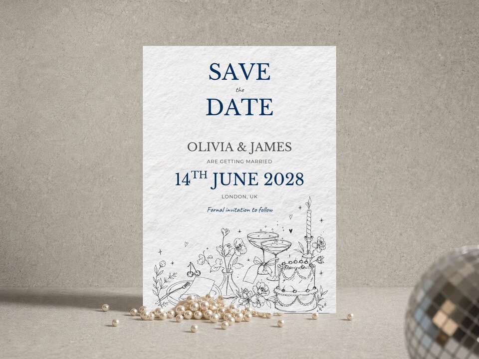 Save the date card featuring blue text and botanical illustrations, displayed on a textured surface with pearls and a partial disco ball.