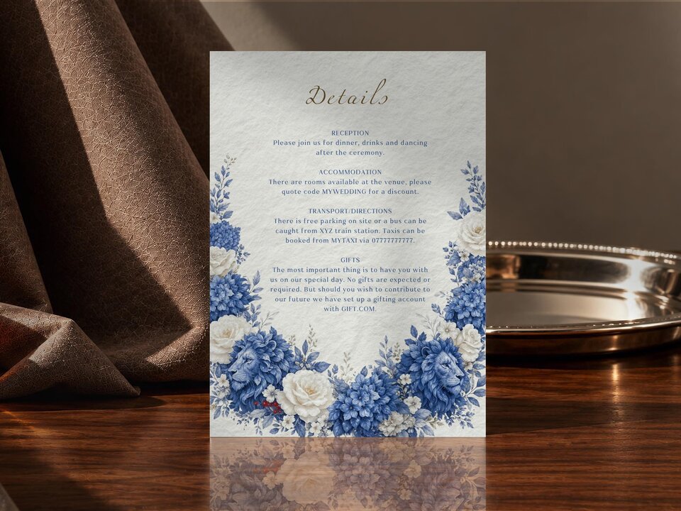 A wedding details card with blue floral and lion motifs is displayed vertically on a dark wooden surface.