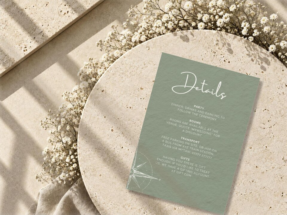 A sage green details card with white text rests on a round textured stone surface decorated with white baby breath flowers.