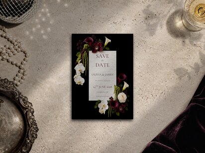 Burgundy and chartreuse floral save the date template shown on a grey surface with editorial flower artwork, pearl necklace and silver tray. Flowers include burgundy calla lilies, burgundy cymbidium orchids, white orchids, ivory roses and trailing amaranthus with chartreuse accents