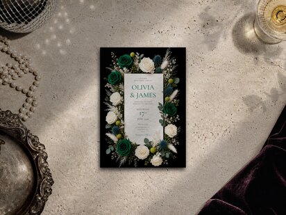 Emerald green roses, ivory roses, blue thistle, craspedia (billy buttons), pampas plumes and eucalyptus wedding invitation template shown on a grey surface with editorial flower artwork, pearl necklace and silver tray.