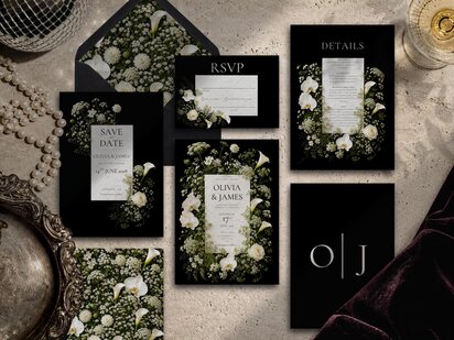 A flat lay of a black-and-white floral wedding invitation suite including a save-the-date, RSVP, and details cards surrounded by pearls and an open envelope.