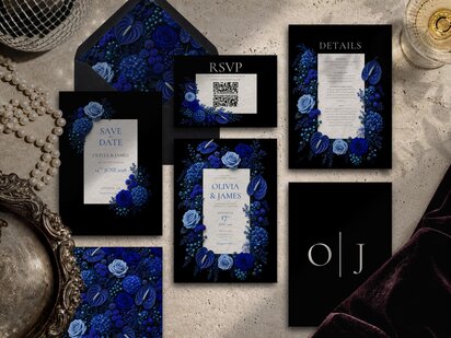 A flat lay arrangement of a wedding invitation suite with black backgrounds and cobalt blue floral illustrations on a textured stone surface.